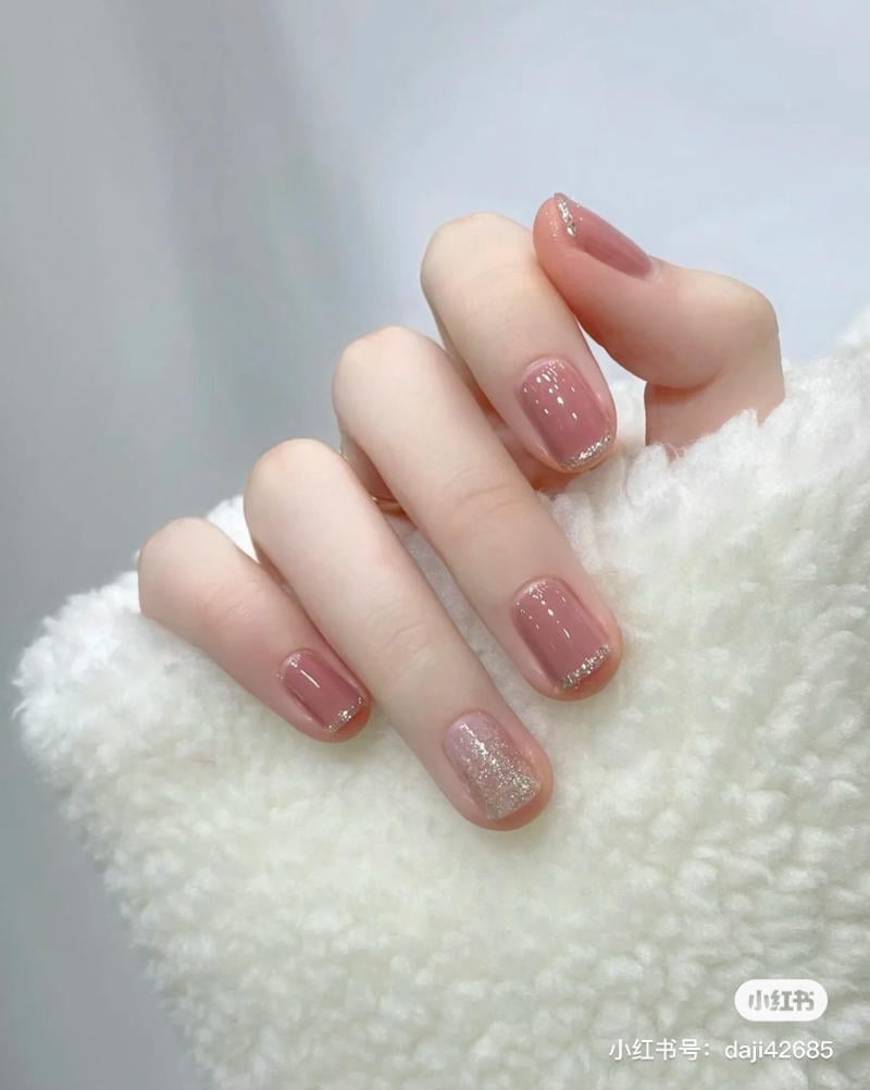 mau-nail-don-gian-cardina__146__e894879c496745e4b2a6fd786f28b98e Bàn tay với móng tay được sơn màu hồng nhạt và ánh kim, đặt trên nền vải trắng mềm mại.