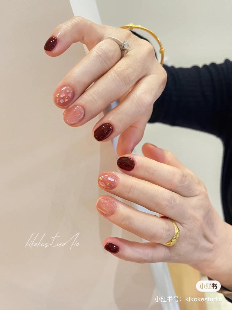 mau-nail-don-gian-cardina__23__aa4ccd542f0a477481427299f2574756 Bàn tay với móng tay được sơn màu đỏ và hồng, có trang trí họa tiết lấp lánh, đeo nhẫn và vòng tay.