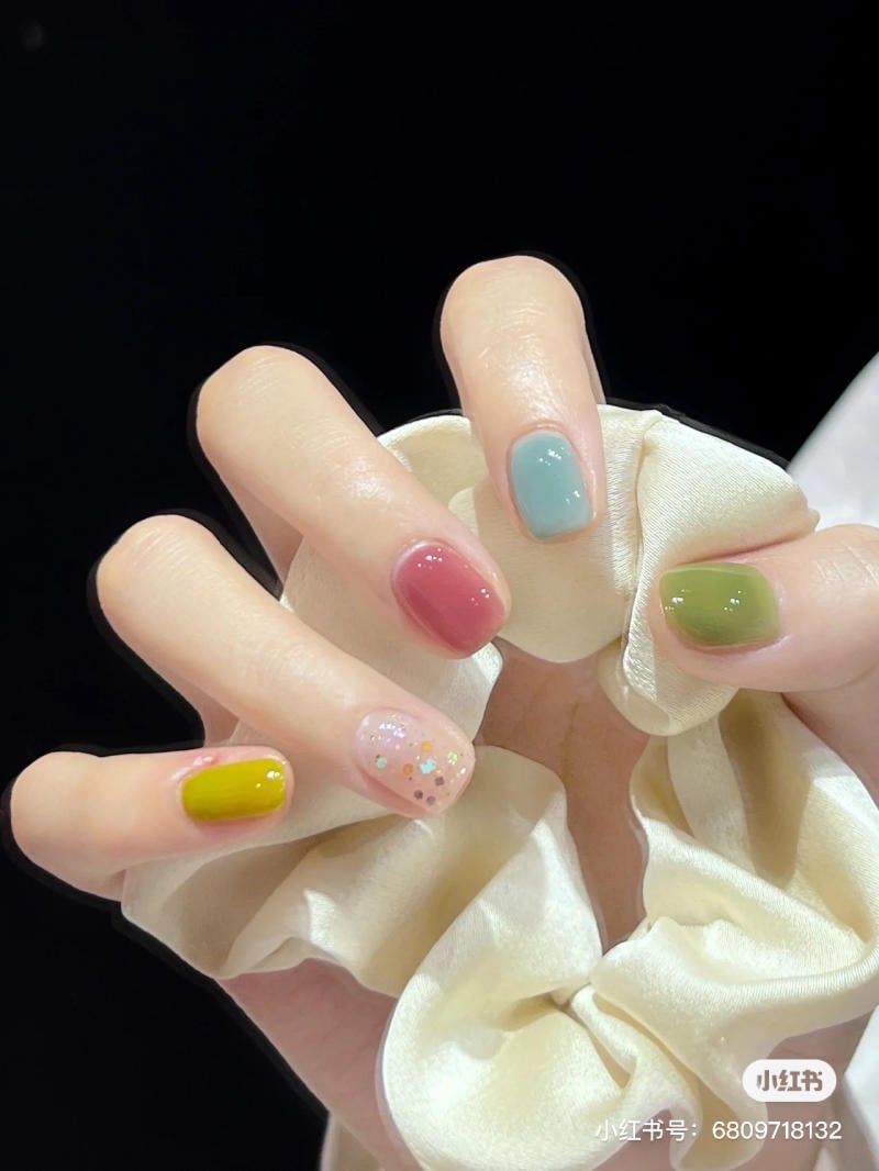 mau-nail-don-gian-cardina__5__500a645dbe2143a599cdf8b768ef3a32 Bàn tay với móng tay sơn nhiều màu sắc khác nhau, cầm một chiếc dây buộc tóc màu kem.