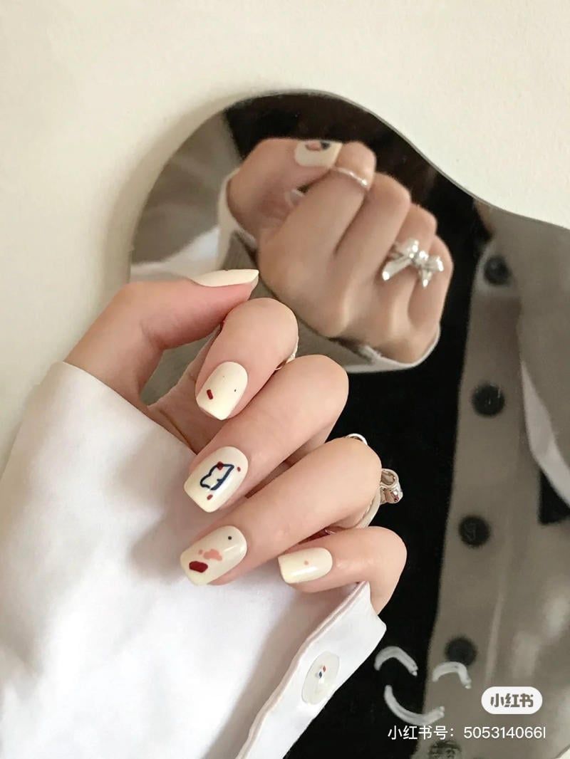 mau-nail-don-gian-cardina__66__b7b8f092fab048789f94b009de68ad9a Tay với móng tay sơn màu trắng, họa tiết đơn giản, phản chiếu trong gương tròn nhỏ.