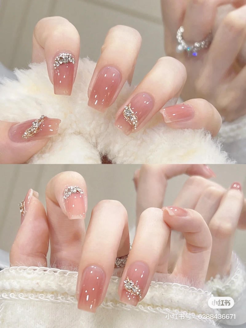mau-nail-don-gian-cardina__72__1ed5da662e4e40f1b3c8ac31867d0e26 Bàn tay với móng tay sơn màu hồng nhạt, trang trí đá lấp lánh trên nền vải trắng.