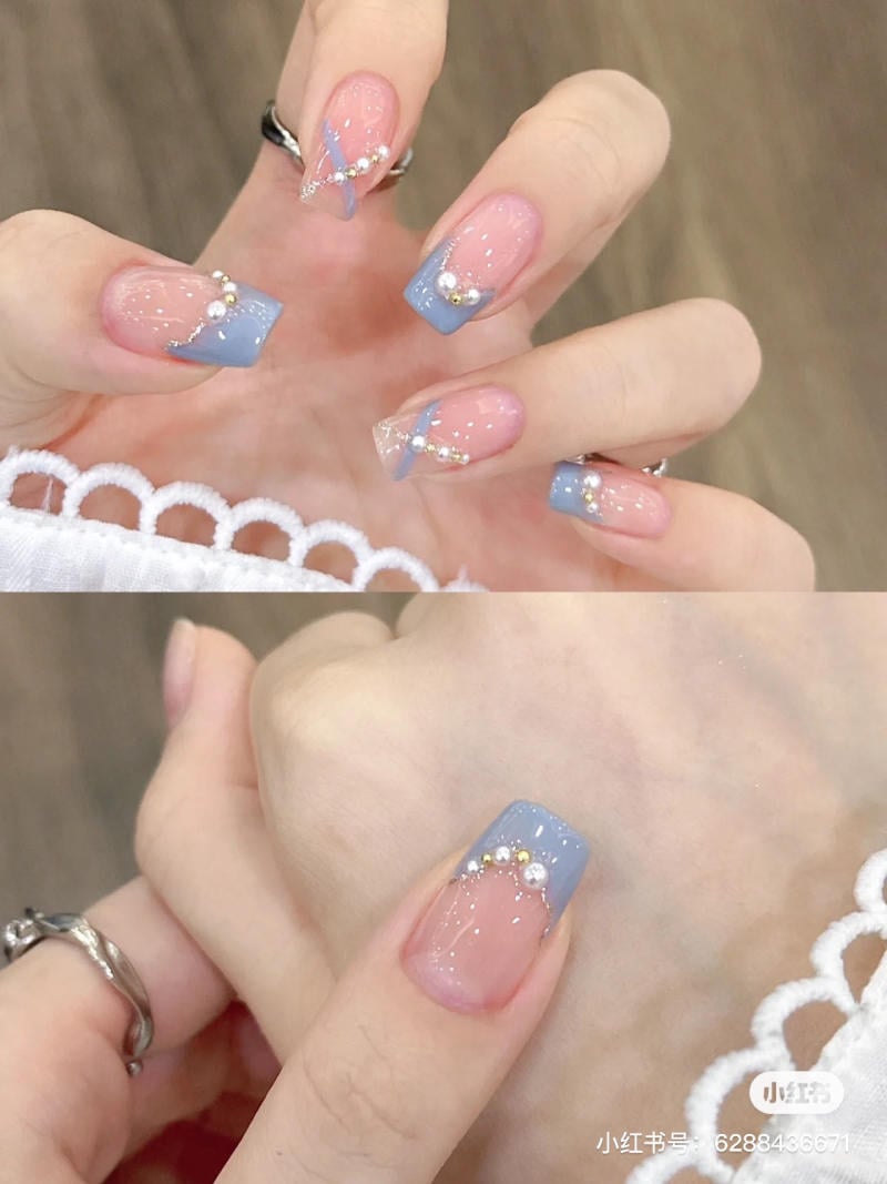 mau-nail-don-gian-cardina__77__1c0822d3f6524e2eba657bbeab888ebf Bàn tay với móng tay sơn màu xanh và hồng, trang trí đá và ngọc trai nhỏ, trên nền gỗ.