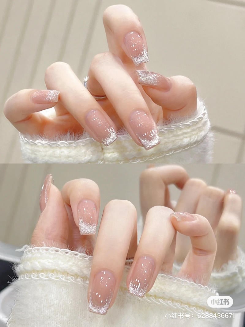 mau-nail-don-gian-cardina__78__4e8a816e34ee47b4a9c2fd22036817e6 Bàn tay với móng tay sơn màu nude và đầu móng lấp lánh, mặc áo len trắng.