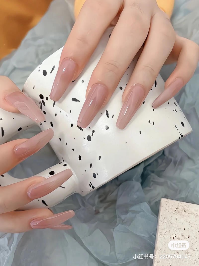 mau-nail-don-gian-cardina__79__517431bc65e94ed8a51a028529678a6e Bàn tay với móng tay dài màu nude đang cầm một chiếc cốc trắng có hoa văn đen.
