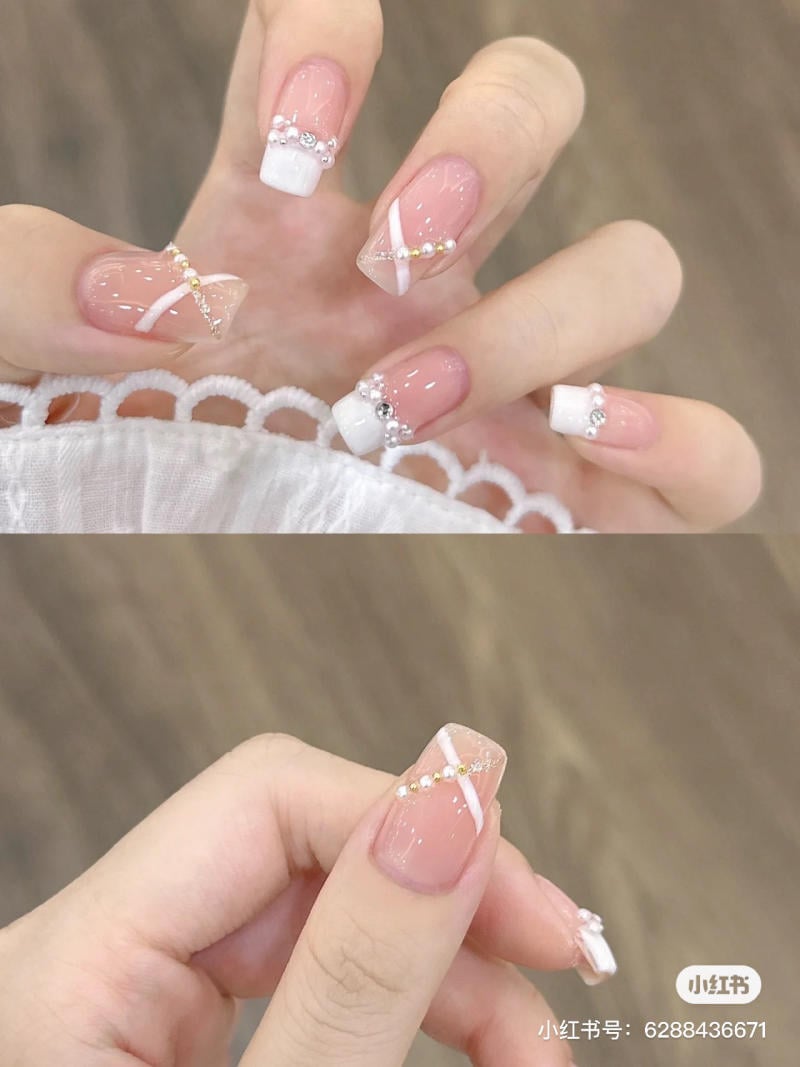 mau-nail-don-gian-cardina__80__8e1efc67452c4c39b6679370a53cdf3a Bàn tay với móng tay được trang trí bằng sơn màu hồng nhạt, đính đá và họa tiết trắng tinh tế.