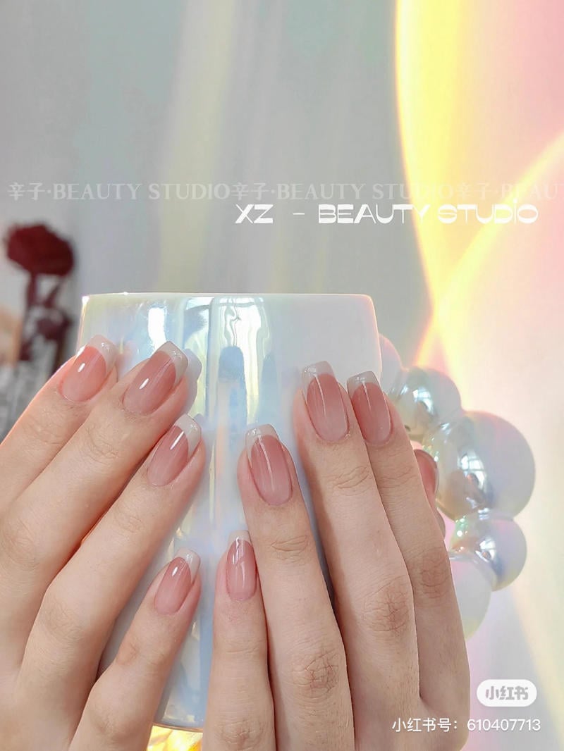 mau-nail-don-gian-cardina__92__5565b6794b0846deb9175511d09eec48 Hai bàn tay có móng sơn màu tự nhiên đang cầm một chiếc cốc trắng, nền ánh sáng dịu nhẹ.