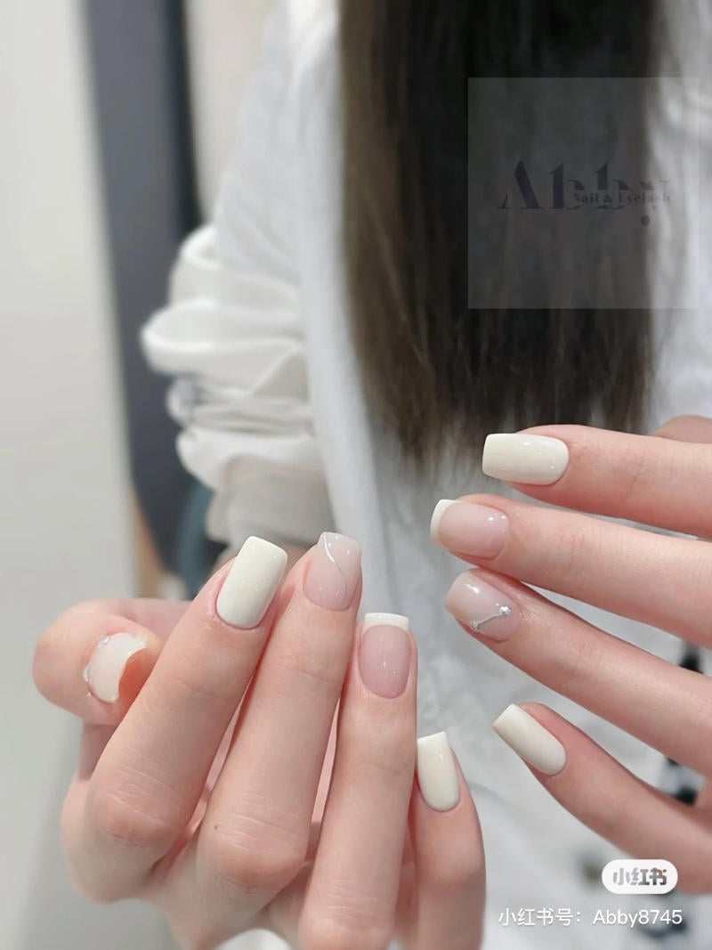 mau-nail-don-gian-cardina__93__57f8bbdc9a894c30bcd1c2826f4c0e80 Bàn tay với móng tay sơn trắng và trong suốt, thiết kế đơn giản và tinh tế, trên nền áo trắng.