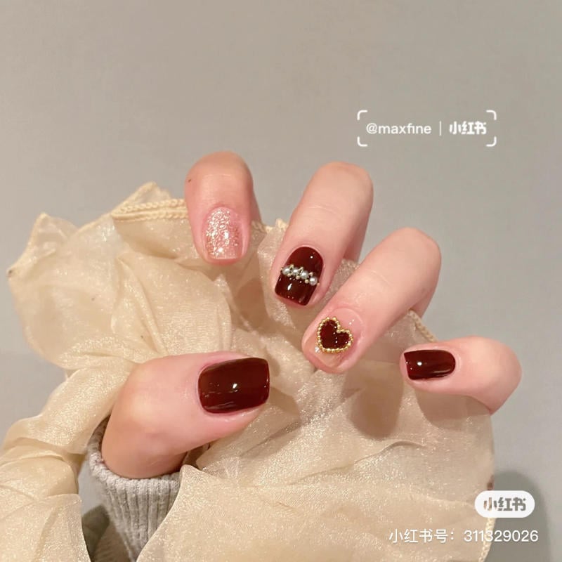 Bàn tay với móng tay sơn màu đỏ thẫm và trang trí kim tuyến, hạt cườm, hình trái tim nhỏ.