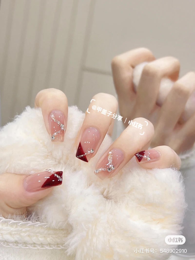 Bàn tay với móng tay được trang trí bằng họa tiết đỏ và kim tuyến, cầm một vật liệu lông mềm mịn.