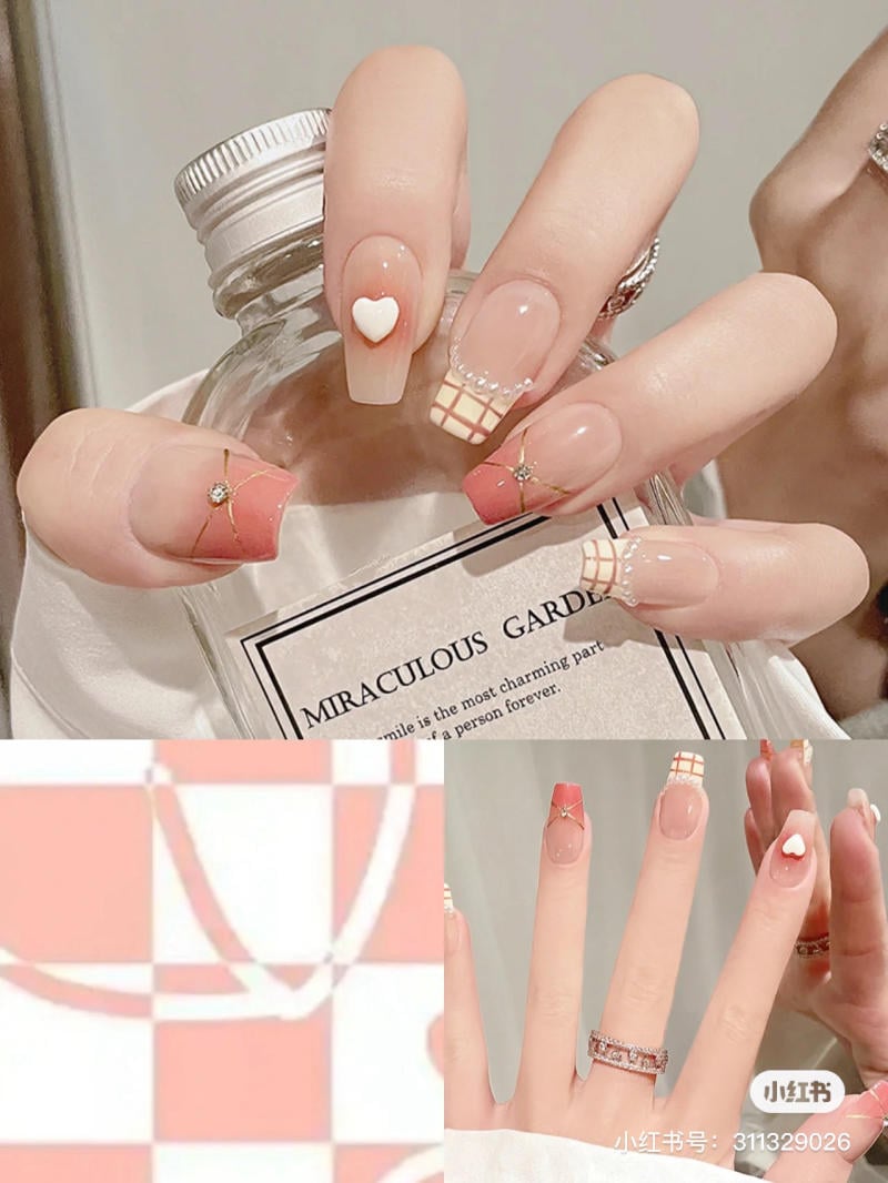 Bàn tay với móng tay được trang trí họa tiết caro và trái tim, cầm chai nước hoa trong nền màu hồng.