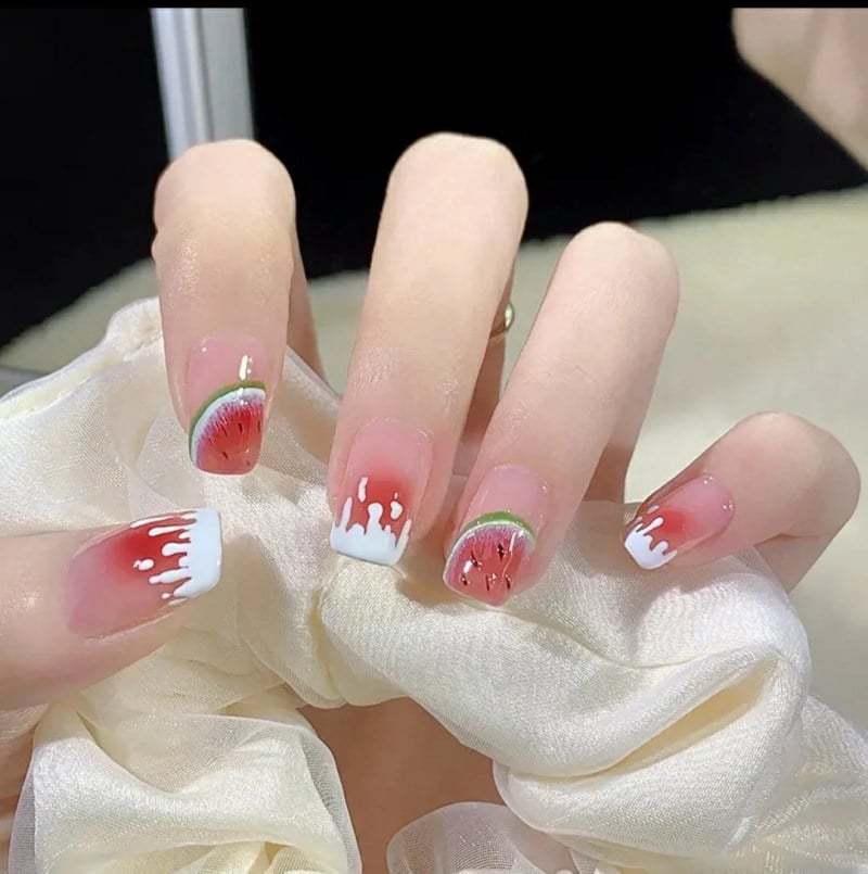 Bàn tay với móng tay được sơn họa tiết dưa hấu đỏ và trắng, kết hợp với khăn tay màu trắng.