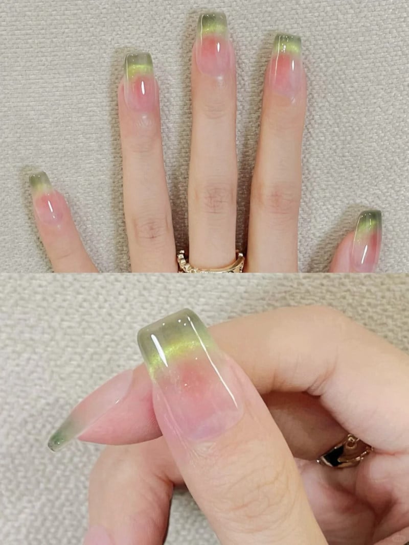 Bàn tay với móng tay sơn ombre màu xanh lá cây và hồng, đeo nhẫn vàng trên ngón tay giữa.