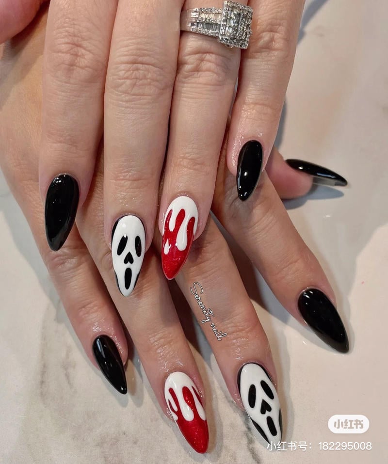 mau-nail-halloween-2023__10__6ff9592de67e416bbfcac86e98eeaeab Bàn tay với móng tay sơn đen, trắng và đỏ, họa tiết giọt và mặt nạ, đeo nhẫn kim cương.
