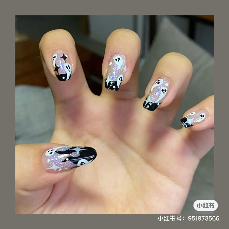 mau-nail-halloween-2023__11__6fa0709fd5494681ab8fa916416e5b92 Bàn tay với móng tay vẽ hình ma nhỏ trên nền đen và bạc lấp lánh, phong cách nghệ thuật Halloween.