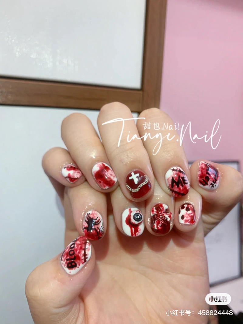 mau-nail-halloween-2023__13__e086de5053e94534bbea47797ac96da6 Bàn tay với móng tay được trang trí theo chủ đề Halloween, bao gồm họa tiết máu và hình ảnh đáng sợ.