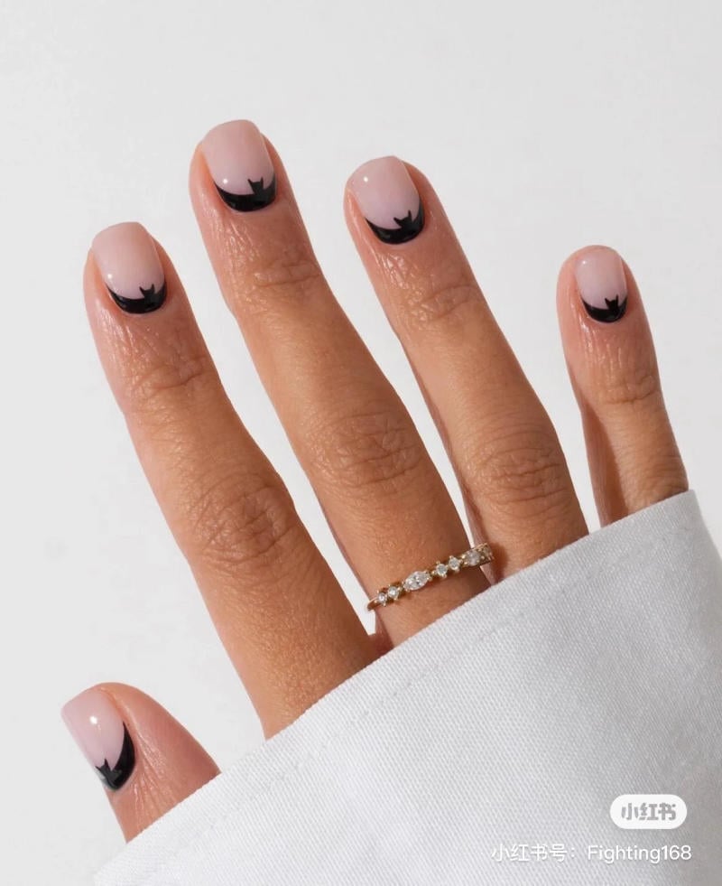 mau-nail-halloween-2023__16__7f822251f8eb419685a462fefc8b6bc5 Bàn tay đeo nhẫn với móng tay sơn màu hồng nhạt, đầu móng có họa tiết đen hình răng cưa.
