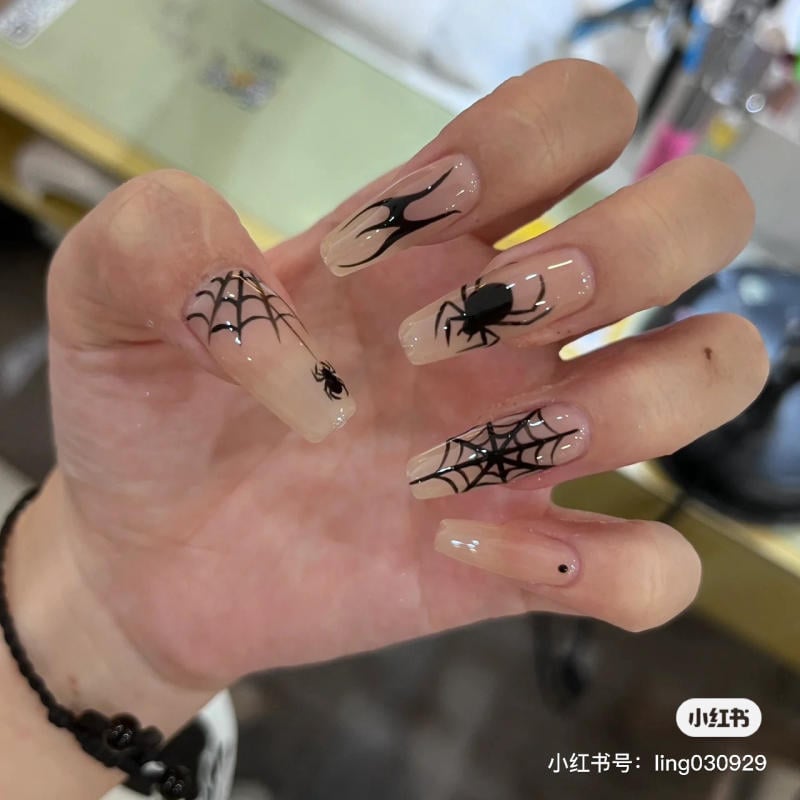 mau-nail-halloween-2023__17__500d58fd0d6c4c91bd43317ebc0ae3bf Bàn tay với móng tay dài, trang trí hình mạng nhện và nhện đen trên nền màu nude.