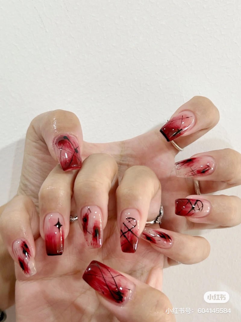 mau-nail-halloween-2023__19__0d4e0b576b334ed0baa0e755731032e1 Bàn tay với móng tay được sơn màu đỏ và đen, thiết kế nghệ thuật tinh tế trên nền trắng.