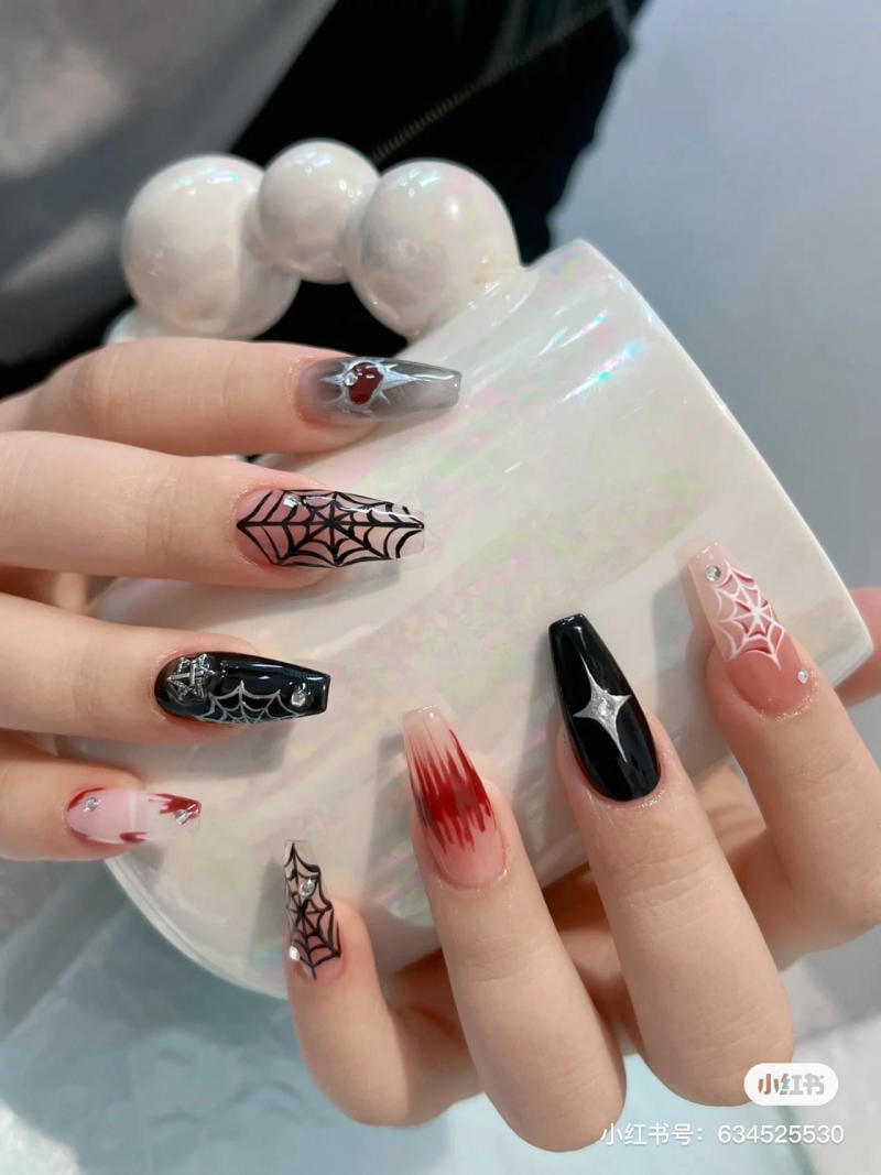 mau-nail-halloween-2023__1__be79cc4451334f3aa37403d8ae21016f Bàn tay với móng tay thiết kế họa tiết mạng nhện và màu sắc đa dạng cầm một chiếc túi sáng bóng.