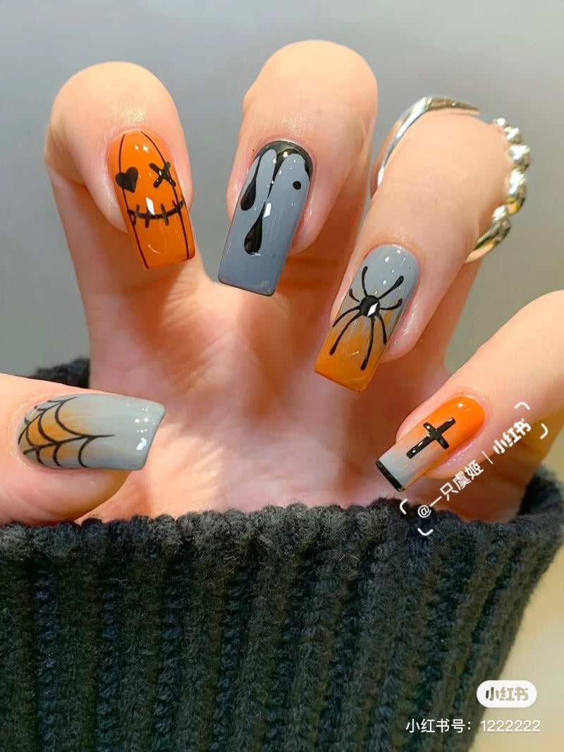 mau-nail-halloween-2023__4__9e297aee61b142cd8bf6aecc64e7c742 Bàn tay với móng tay trang trí họa tiết Halloween, gồm mặt cười, mạng nhện, giọt nước, nhện và thánh giá.