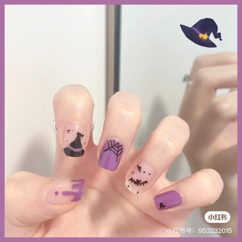 mau-nail-halloween-dep__11__913392dec16a427ca4d3de9f07adeb10 Bàn tay với móng tay trang trí chủ đề Halloween, gồm hình mũ phù thủy, mạng nhện và dơi, màu tím và đen.