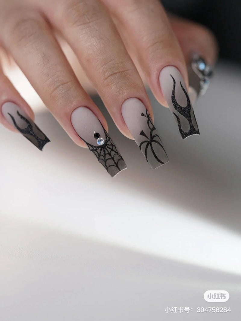 mau-nail-halloween-dep__12__948da76d878b4fcd83dd45e74503174c Bàn tay với móng tay trang trí họa tiết mạng nhện và hoa văn đen, đính đá nhỏ sáng bóng.