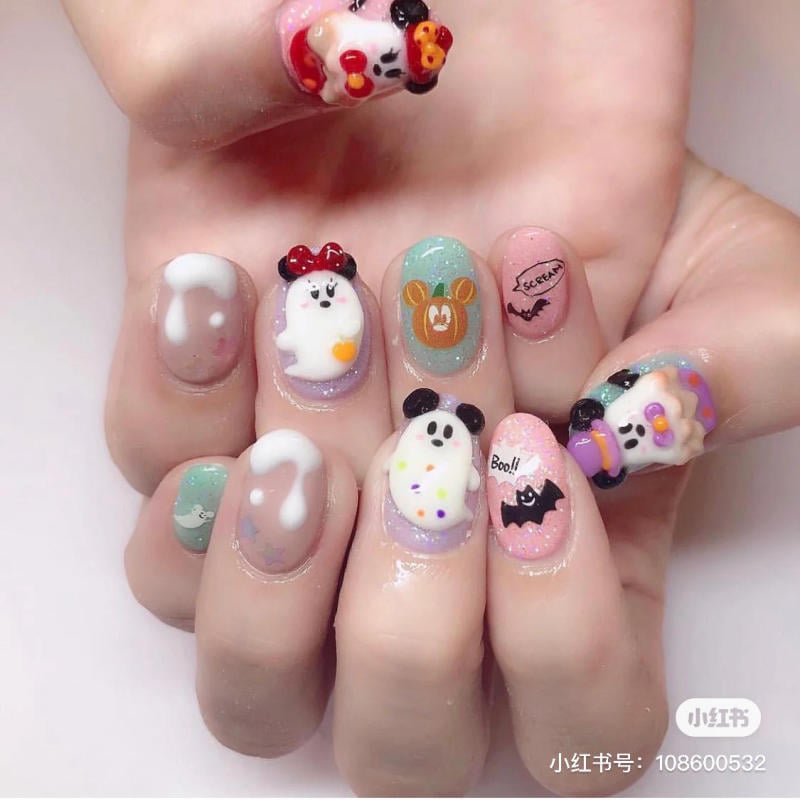 mau-nail-halloween-dep__15__424323b7b6594545b20d9c2a10e0371b Bàn tay với móng tay trang trí hình ma và nhân vật dễ thương trên nền màu sắc tươi sáng.