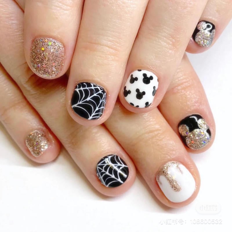 mau-nail-halloween-dep__18__b9d947fd29f94cd9b9c03622f726aaf3 Bàn tay với móng tay được trang trí đa dạng, kết hợp họa tiết mạng nhện, hình đầu chuột và ánh kim lấp lánh.