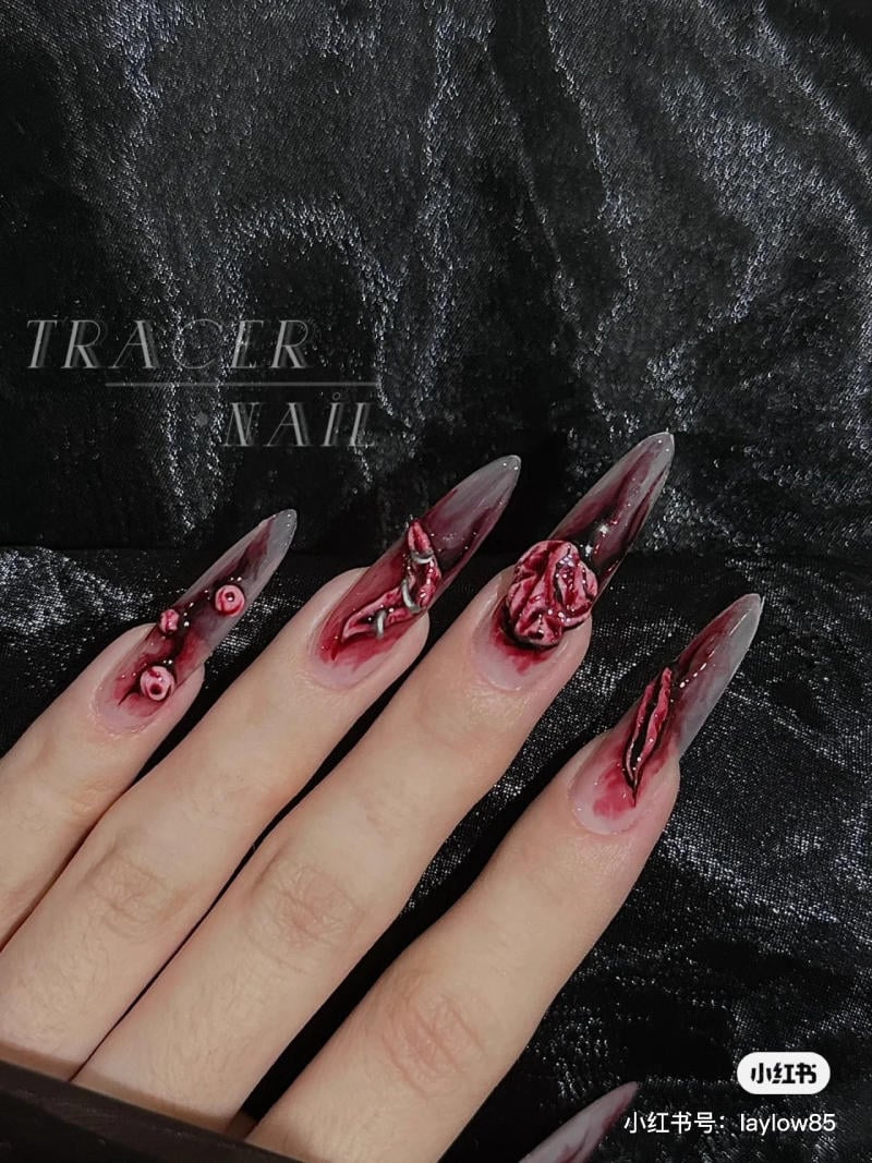 mau-nail-halloween-dep__19__cc6f15a1d43745a7ab971272e27ef863 Bàn tay với móng tay dài, được trang trí nghệ thuật với hoa văn màu đỏ trên nền đen.