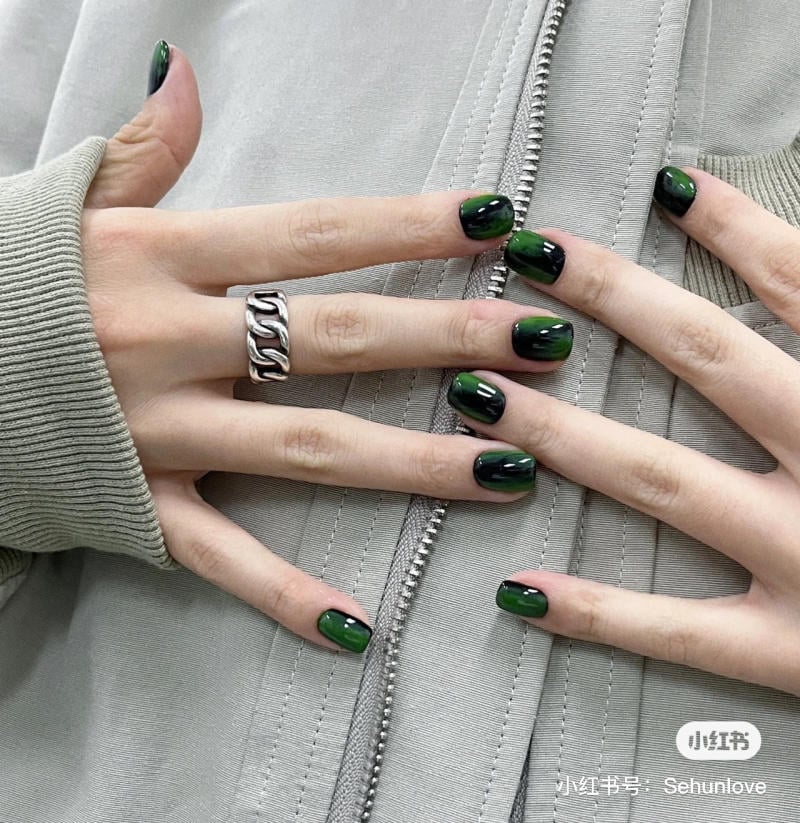 mau-nail-halloween-dep__20__c704bfcd79fd4276a0fc864978d0af41 Bàn tay với móng tay sơn màu xanh đen, đeo nhẫn bạc, đặt trên áo khoác màu xám.
