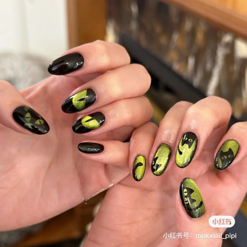 mau-nail-halloween-dep__22__ad61b3bba11e4f97a7b4eef82c9429be Bàn tay với móng tay sơn màu đen và xanh lục, trang trí họa tiết kỳ bí trên nền sáng.