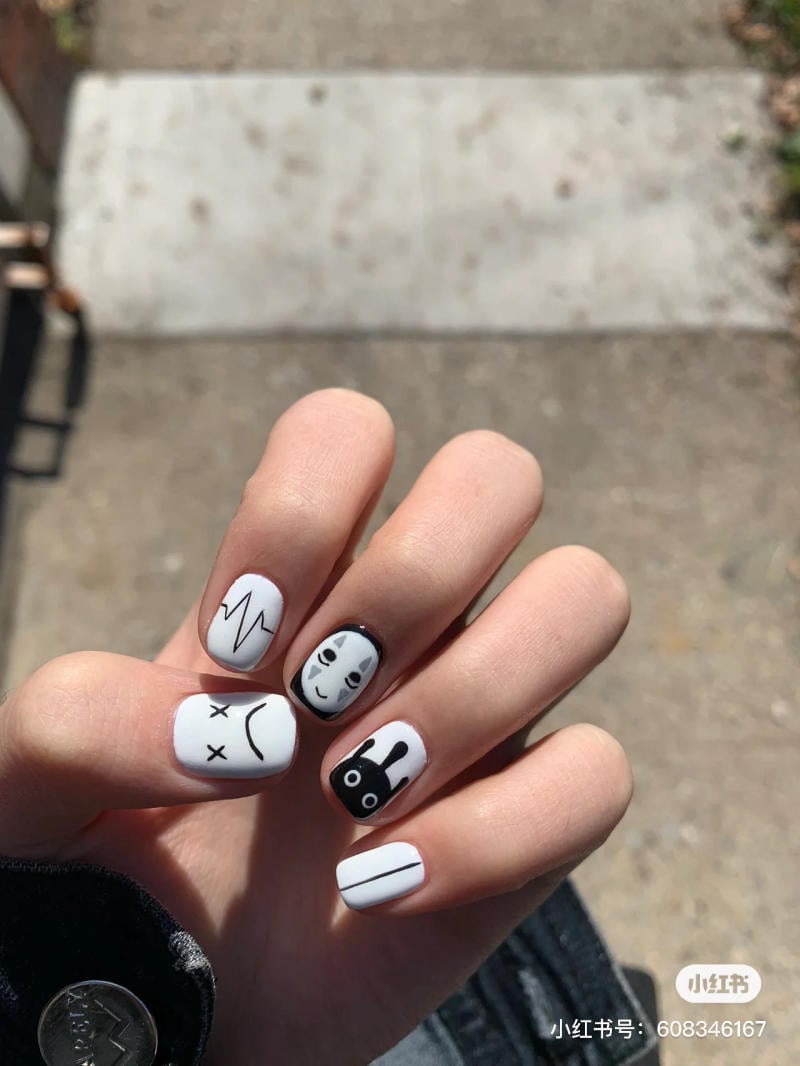 mau-nail-halloween-dep__23__875cc351536f49118c95a9dae798b884 Bàn tay với móng tay sơn hình vẽ trắng đen độc đáo, có các biểu tượng và hình ảnh khác nhau.
