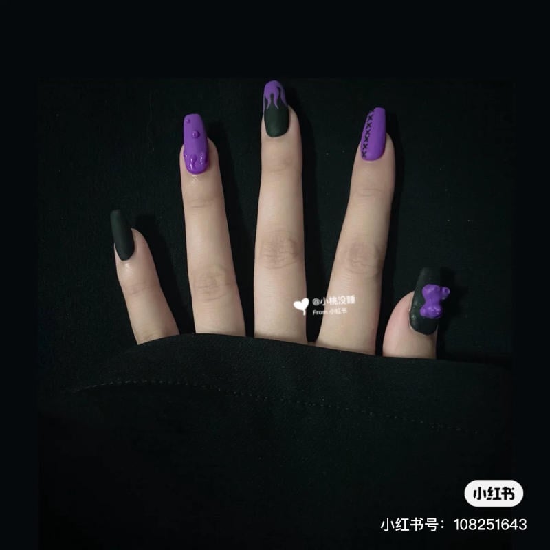 mau-nail-halloween-dep__26__12d27afa1d7c4506ac9ccf05d26bd552 Bàn tay với móng tay dài được sơn màu đen và tím, có họa tiết trang trí nổi bật.