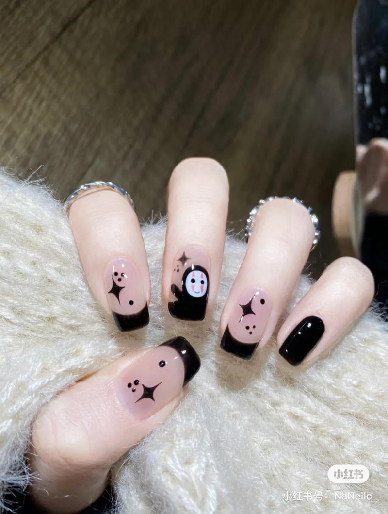 mau-nail-halloween-dep__33__3a7b08ca2fc84ee0aa7b255742f123ad Bàn tay với móng tay sơn đen, họa tiết mặt cười và ngôi sao, trên nền vải lông màu sáng.