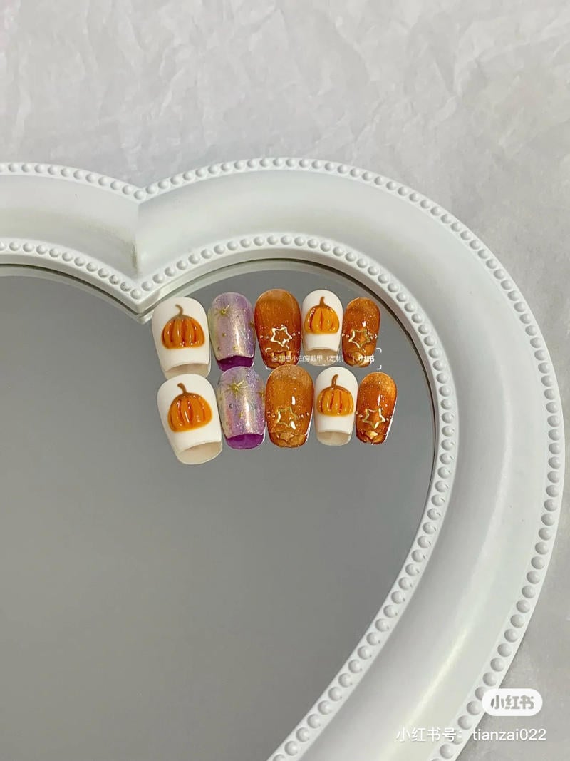 mau-nail-halloween-dep__38__8cca6f10710e4d649eb0c8e6983d40c2 Bộ móng tay giả với họa tiết bí ngô và sao, đặt trên gương hình trái tim viền trắng.
