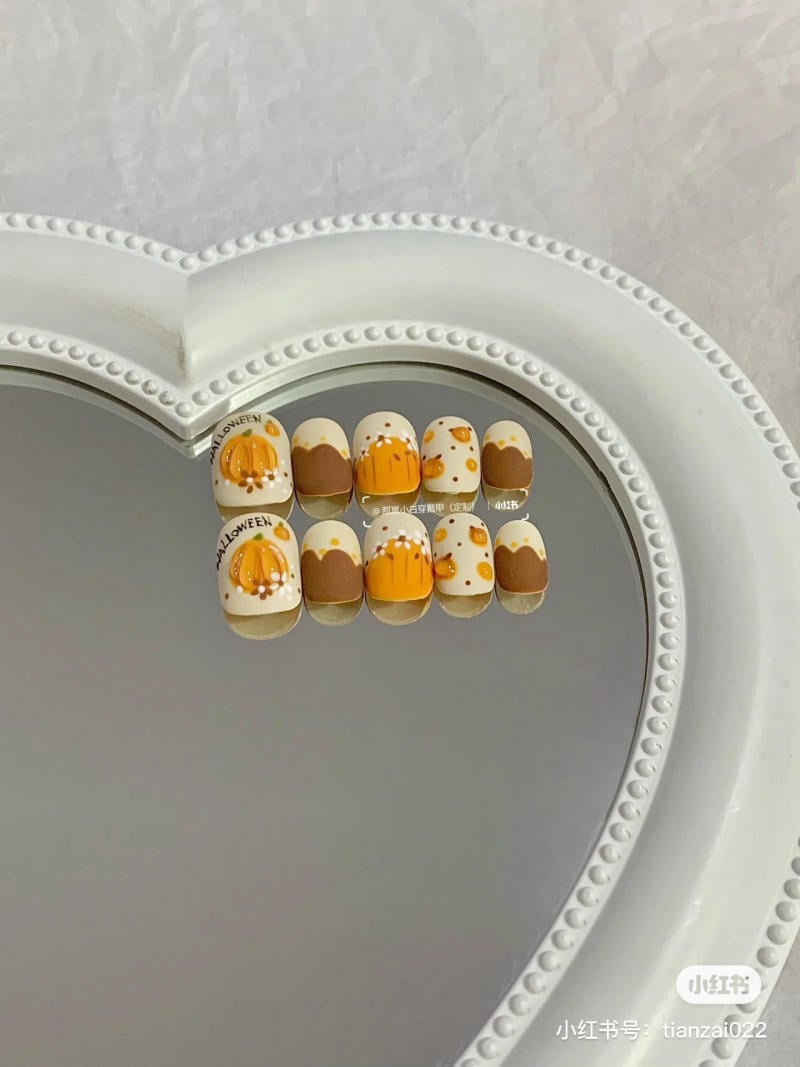 mau-nail-halloween-dep__39__4c625e4bc83044639a156677bde57ec1 Mẫu móng tay trang trí hình bí ngô và chấm bi màu cam-đen trên nền trắng, đặt trên khay gương hình trái tim.
