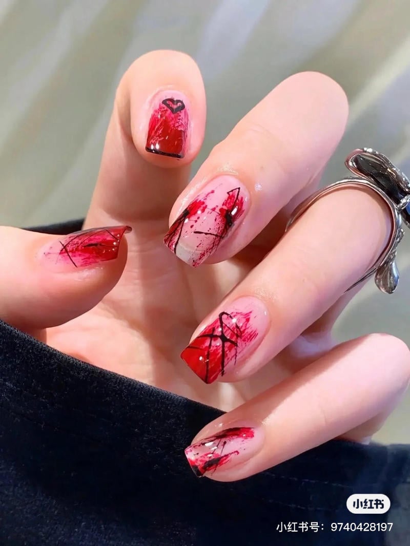 mau-nail-halloween-dep__45__8d149279bb034a078fecf3eb5640cd78 Bàn tay với móng tay được sơn màu đỏ, trang trí họa tiết trái tim và đường kẻ đen nghệ thuật.