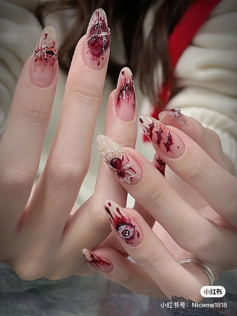 mau-nail-halloween-dep__47__0ccfd43f8f864cdfbe2c3d79e87115e5 Bàn tay với móng tay dài được trang trí bằng họa tiết màu đỏ và phụ kiện kim loại nhỏ.