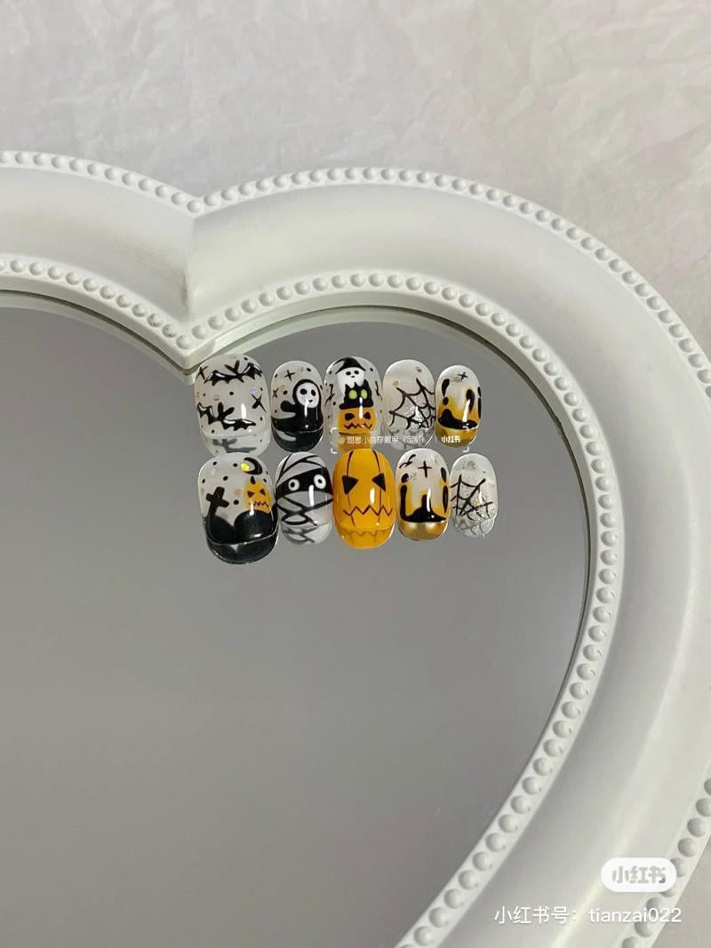 mau-nail-halloween-dep__48__eb63c05634c44b2ea9ed742e91d5f37b Bộ móng tay với họa tiết Halloween, bao gồm bí ngô, mạng nhện và hình ma quái, trên nền gương hình trái tim.