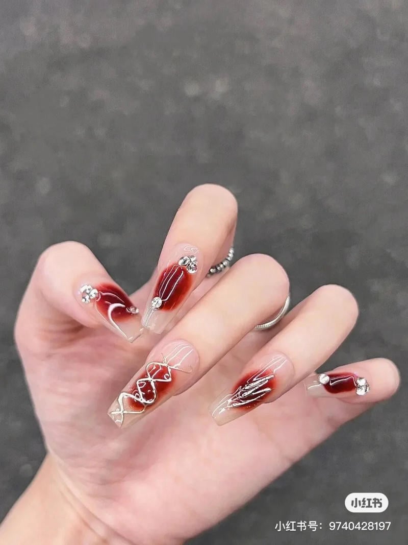 mau-nail-halloween-dep__51__912f287858194d5ab6c0a5eea97d19fa Bàn tay với móng tay dài, được trang trí màu đỏ và bạc, có đính đá và họa tiết nghệ thuật.