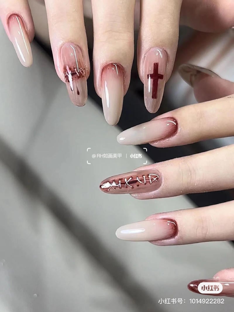 mau-nail-halloween-dep__57__4d7b6bcbe6054997a876bc7a76bb672f Bàn tay với móng tay dài được sơn màu hồng nhạt, có họa tiết chữ và hình thánh giá màu đỏ.