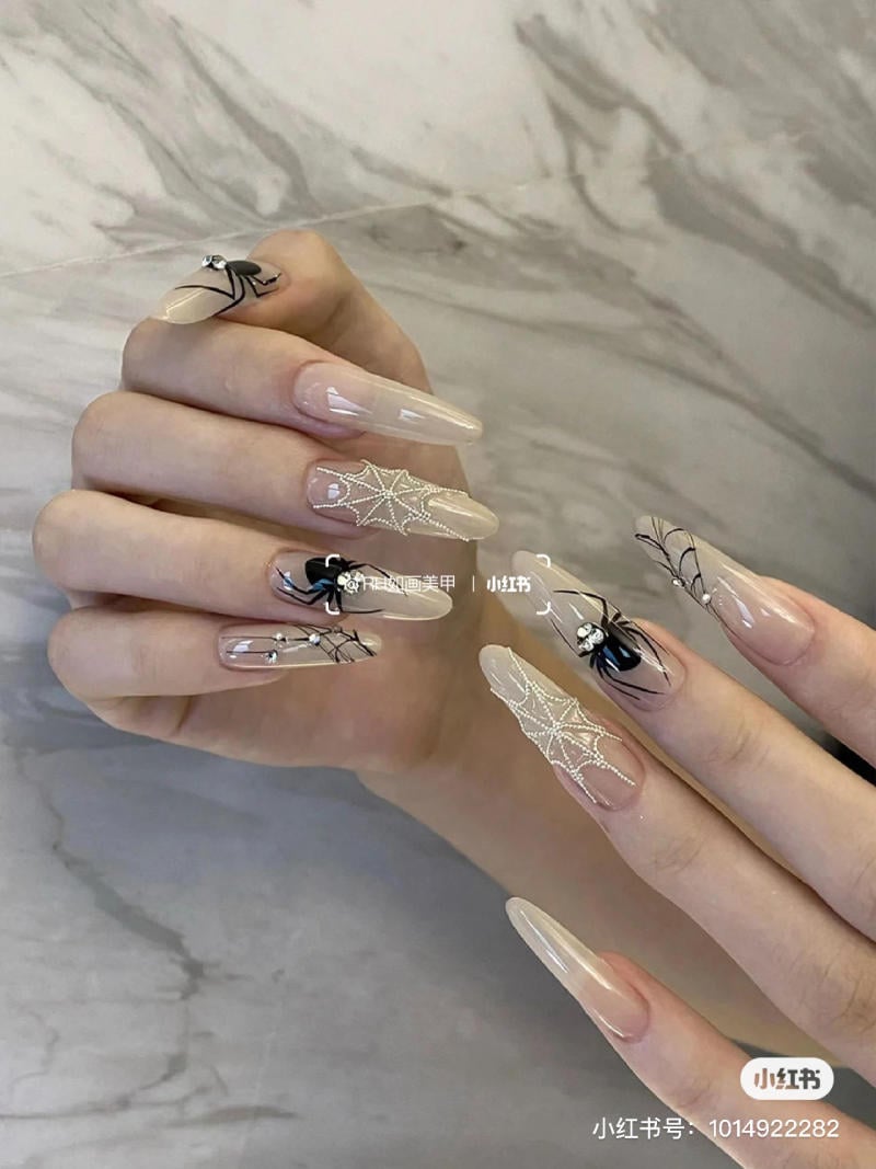 mau-nail-halloween-dep__58__caf4ad7a02d34566a71c67ca765f10a9 Bàn tay với móng tay dài được trang trí họa tiết mạng nhện và nhện trên nền màu nude.