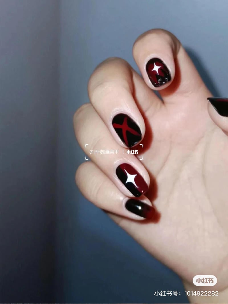 mau-nail-halloween-dep__62__eab56566501940f3a91a633088757056 Ngón tay với móng tay sơn màu đen và đỏ, có họa tiết hình chữ thập và ngôi sao.
