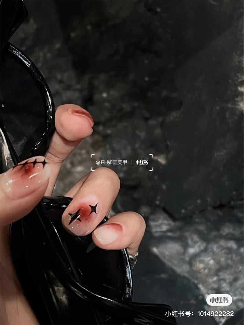 mau-nail-halloween-dep__63__a05760dc933b47cfbf215f4708dde3ce Bàn tay cầm kính đen với móng tay được trang trí họa tiết hoa văn đỏ và sao đen.
