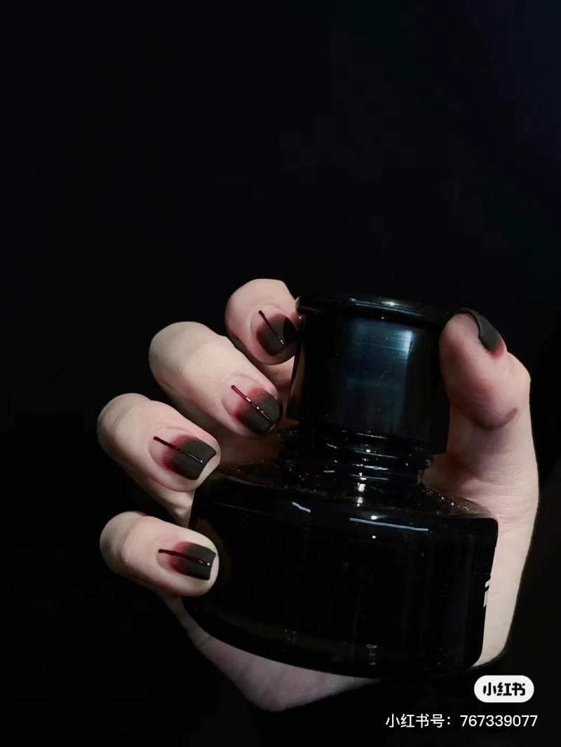 mau-nail-halloween-dep__68__0c90708cdbb0499bb93b524944be888e Bàn tay cầm lọ mực đen, móng tay được sơn màu tối với họa tiết đỏ.