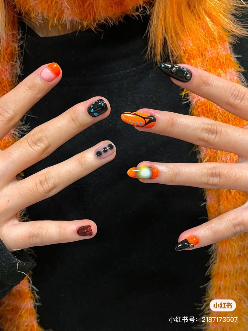 mau-nail-halloween-dep__73__f1575e45d36940f18a4b689a45651a75 Bàn tay với móng tay được trang trí nghệ thuật với các màu sắc và họa tiết đa dạng trên nền đen.