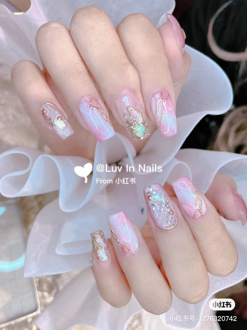 Bàn tay với móng tay được trang trí bằng sơn màu hồng nhạt, họa tiết vân đá và đính đá lấp lánh.