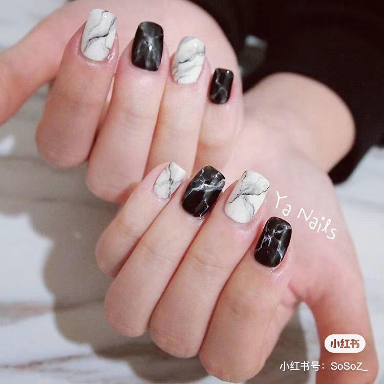 Bàn tay với móng tay sơn màu đen và trắng, họa tiết vân đá cẩm thạch.