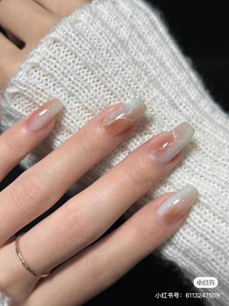 Bàn tay với móng tay sơn màu ombre trắng, đeo nhẫn vàng mỏng, trên nền áo len trắng.