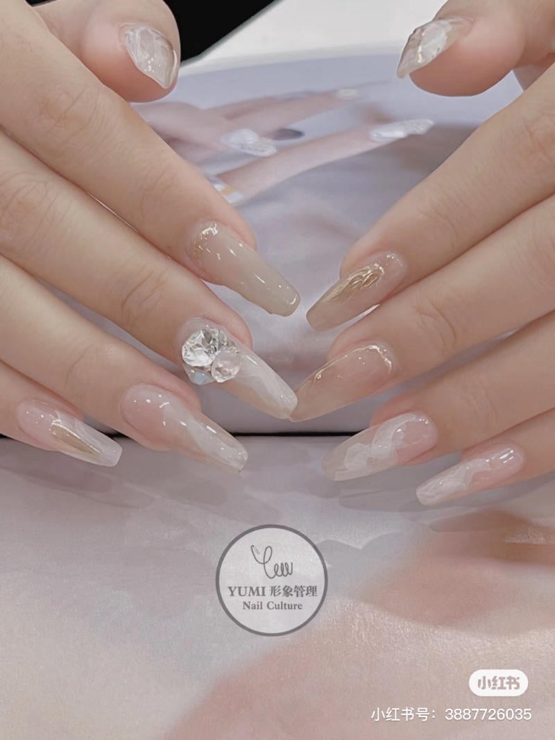 Bàn tay với móng tay dài, trang trí họa tiết và đá sáng bóng, đặt trên nền trắng.